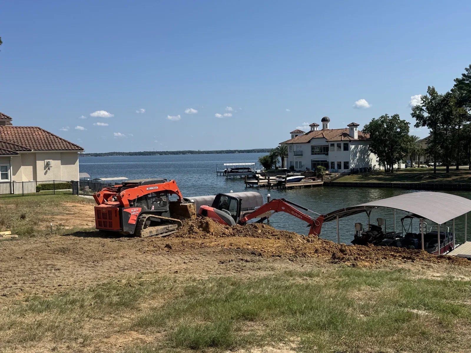 Compact track loader and excavator grading a waterfront lot along the shoreline